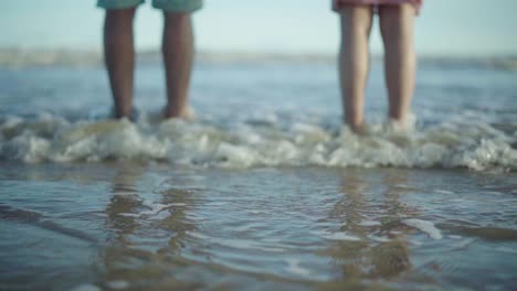 Toma-Borrosa-De-Las-Piernas-De-Una-Pareja-Con-Olas-Golpeando-A-Cámara-Lenta-En-Una-Playa-Vacía