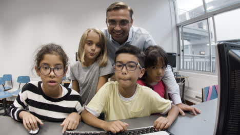 Excited-schoolkid-typing-on-computer-keyboard-while-classmates-and-teacher-watching-at-monitor