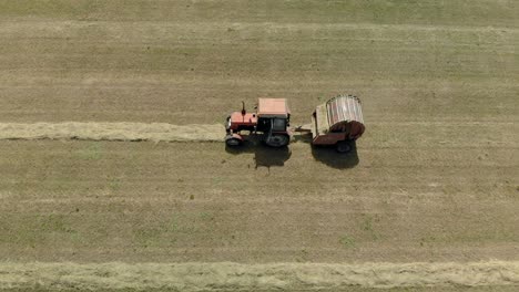vista aérea de un agricultor en un tractor con una balera cosechando heno en un clima soleado y caluroso