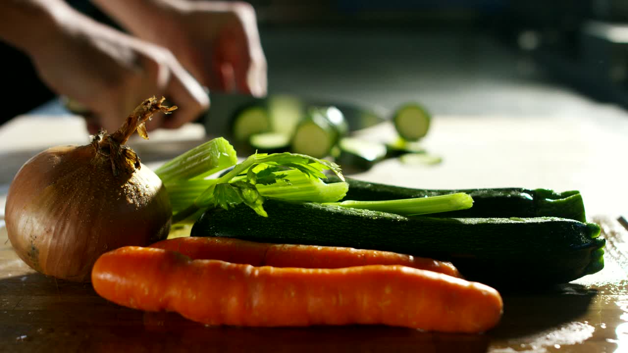 Super slow motion macro of a middle aged chef cutting zucchini with a knife on a wood board
