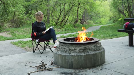 woman reading book beside campfire on camping outdoors vacation