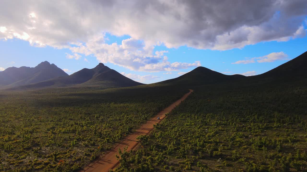 Aerial dolly, car drives down dirt track, lush Australian mountain landscape