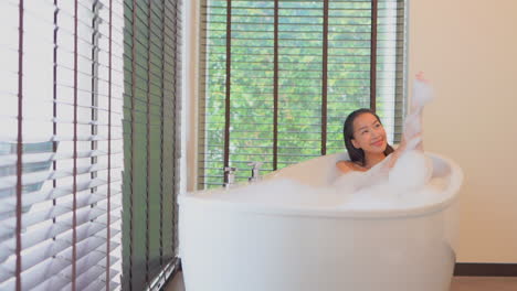 Asian-pretty-model-happy-young-woman-playing-with-foam-in-the-bathtub,-she-is-spreading-foam-on-her-body-and-arms