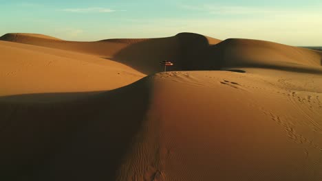 aerial fly by of colorful beach umbrella isolated in desert sand dunes at sunset