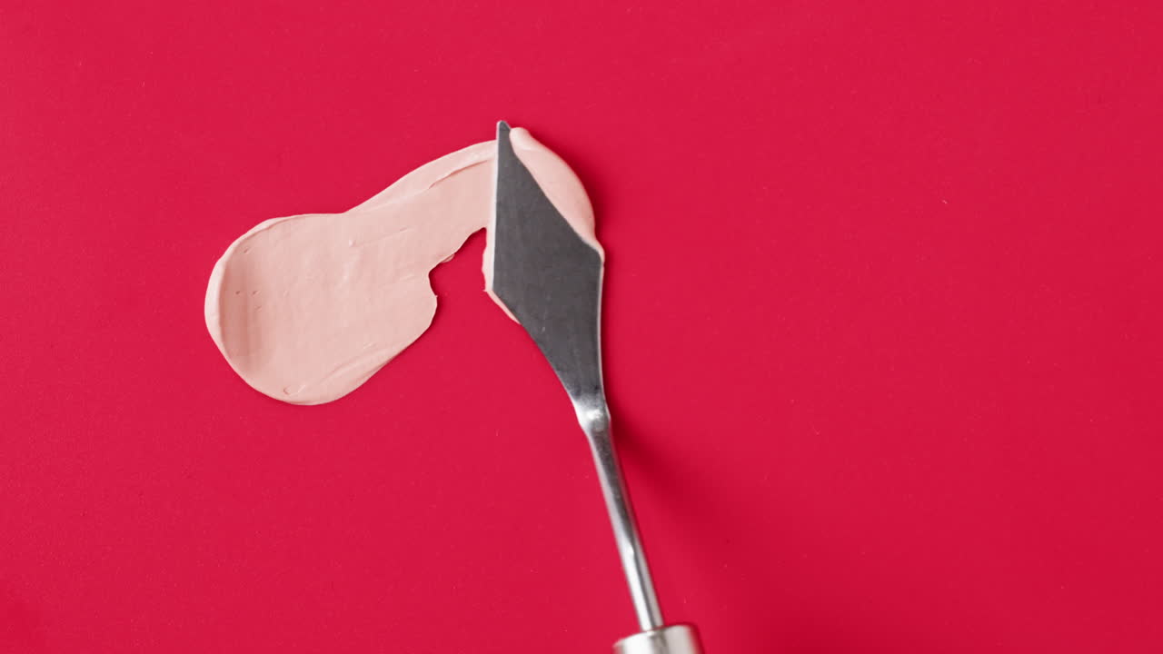 Pink paint being applied with a palette knife on a red surface