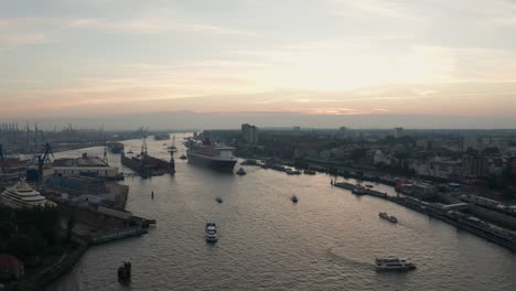 Drohnenaufnahme-Des-Hamburger-Hafens-Queen-Mary-2,-Die-Während-Der-Goldenen-Stunde-Des-Sonnenuntergangs-An-Kreuzfahrttagen-Mit-Skyline-Im-Hintergrund-In-Den-Hafen-Einfährt