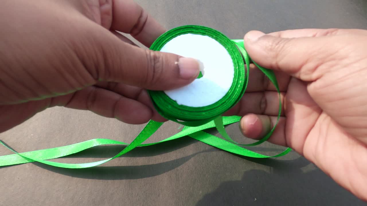 단절된 회색 배경에 손으로 굴러가는 어두운 녹색 롤 사틴 리본의 가까운 부분. 테이블에 물체를 배치하고 배치하십시오.