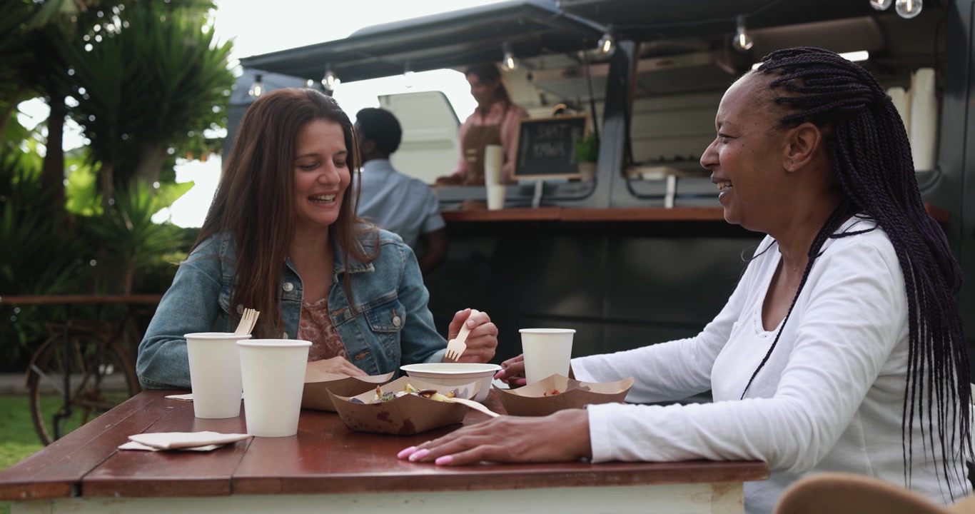 Two Diverse Women Eating and Laughing at a Food Truck