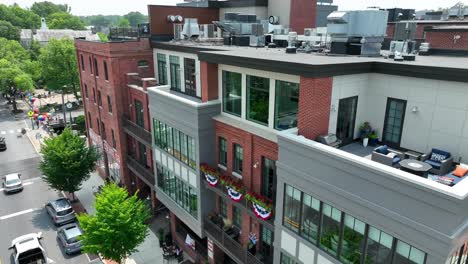 drone view of a condominium complex with amazing outdoor patio areas on a main street lined with mature trees and across the street from a local park area where the pride festival is taking place