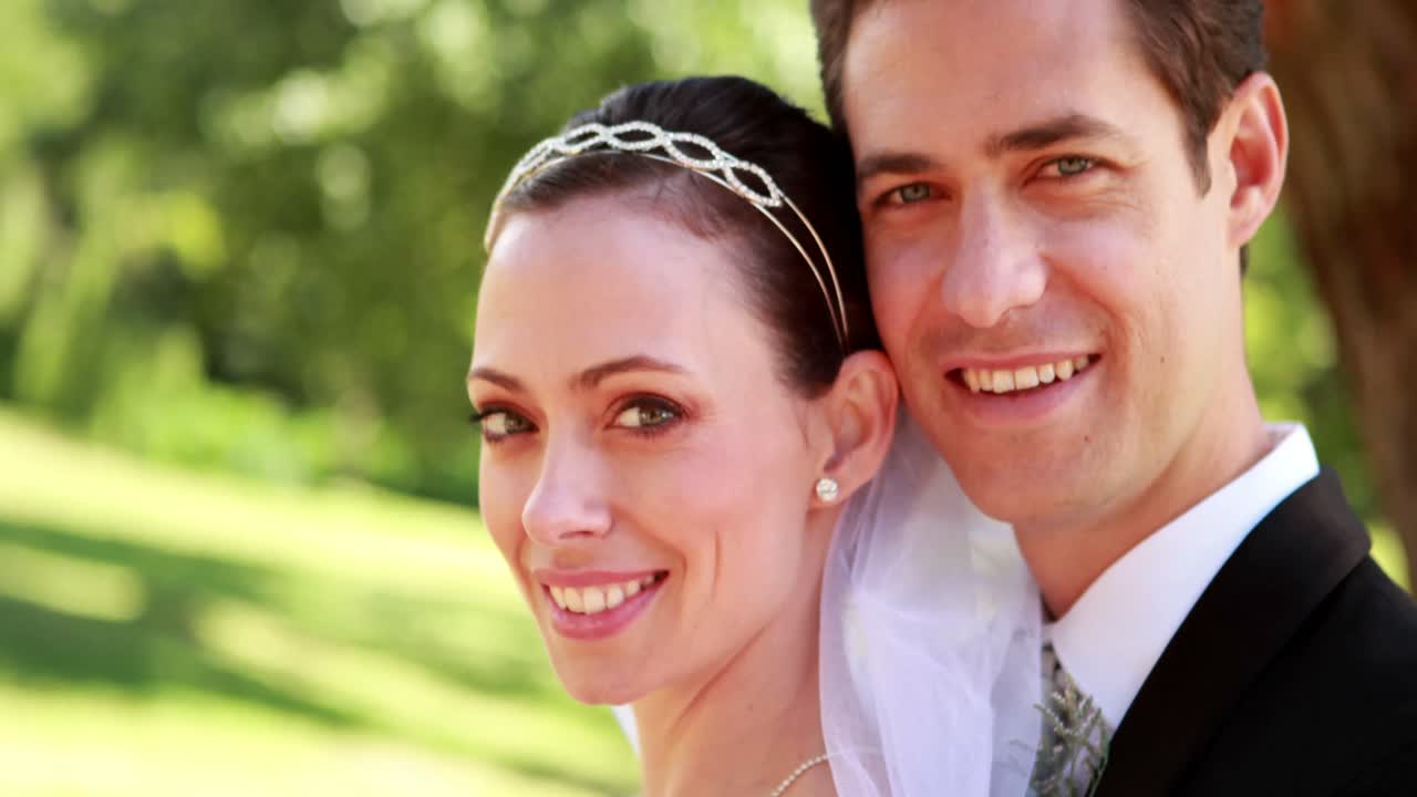 매력적 인 신혼 부부 가 포옹 하는 동안 카메라 에 미소 짓고 있다