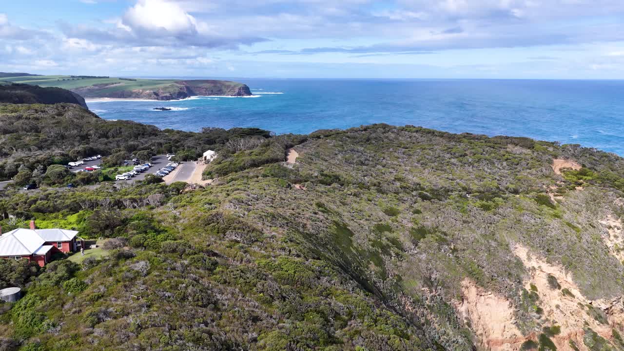 Drone glides past white lighthouse atop rugged cliffs, revealing coastline, ocean, and dramatic landscape