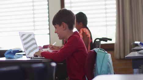 Portrait-of-diverse-schoolchildren-sitting-in-classtoom,-using-laptop,-looking-at-camera,-smiling