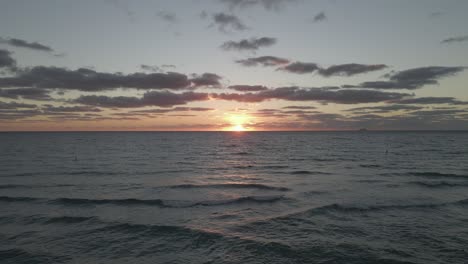 Dramatic-colorful-sunrise-low-on-ocean-horizon,-clouds-in-big-pink-sky