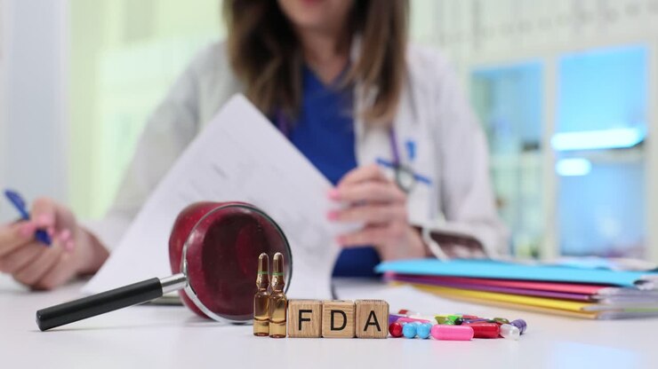 Blocchi di legno compongono l'abbreviazione FDA accanto a un martelletto e compresse in capsule.