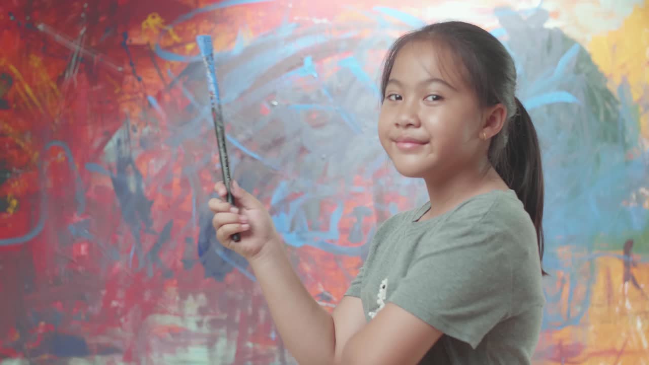 Girl holding paint brush in front of abstract art painting