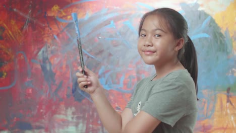 girl holding paint brush in front of abstract art painting
