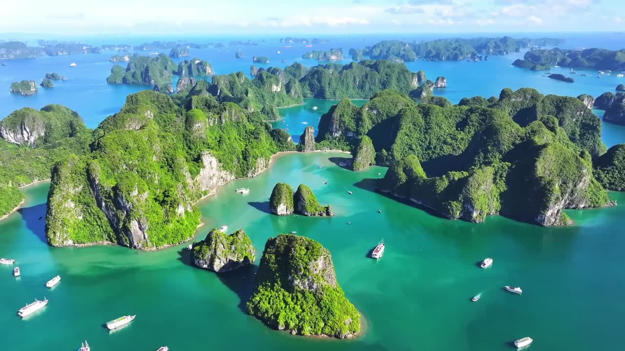 Emerald waters weave through towering limestone islands in Halong Bay, as cruise boats drift peacefully beneath a bright sky, showcasing nature’s grandeur from above.