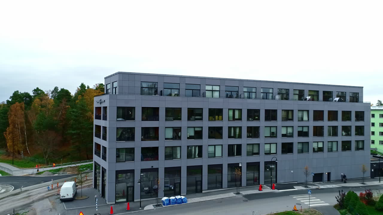 A modern grey office building surrounded by construction and autumn trees