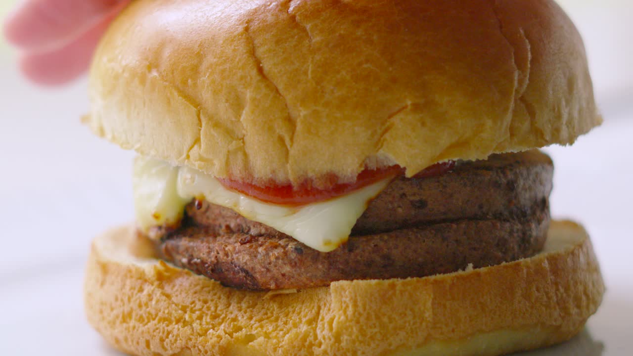 CheeseBurger with Hand Pressing Down so Tomato Ketchup Spills Out Over Cheese in Slow Motion. Freshly Cooked Unhealthy But Delicious Fast Food Eating.