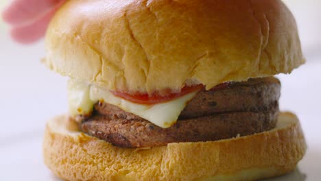 cheeseburger with hand pressing down so tomato ketchup spills out over cheese in slow motion. freshly cooked unhealthy but delicious fast food eating.