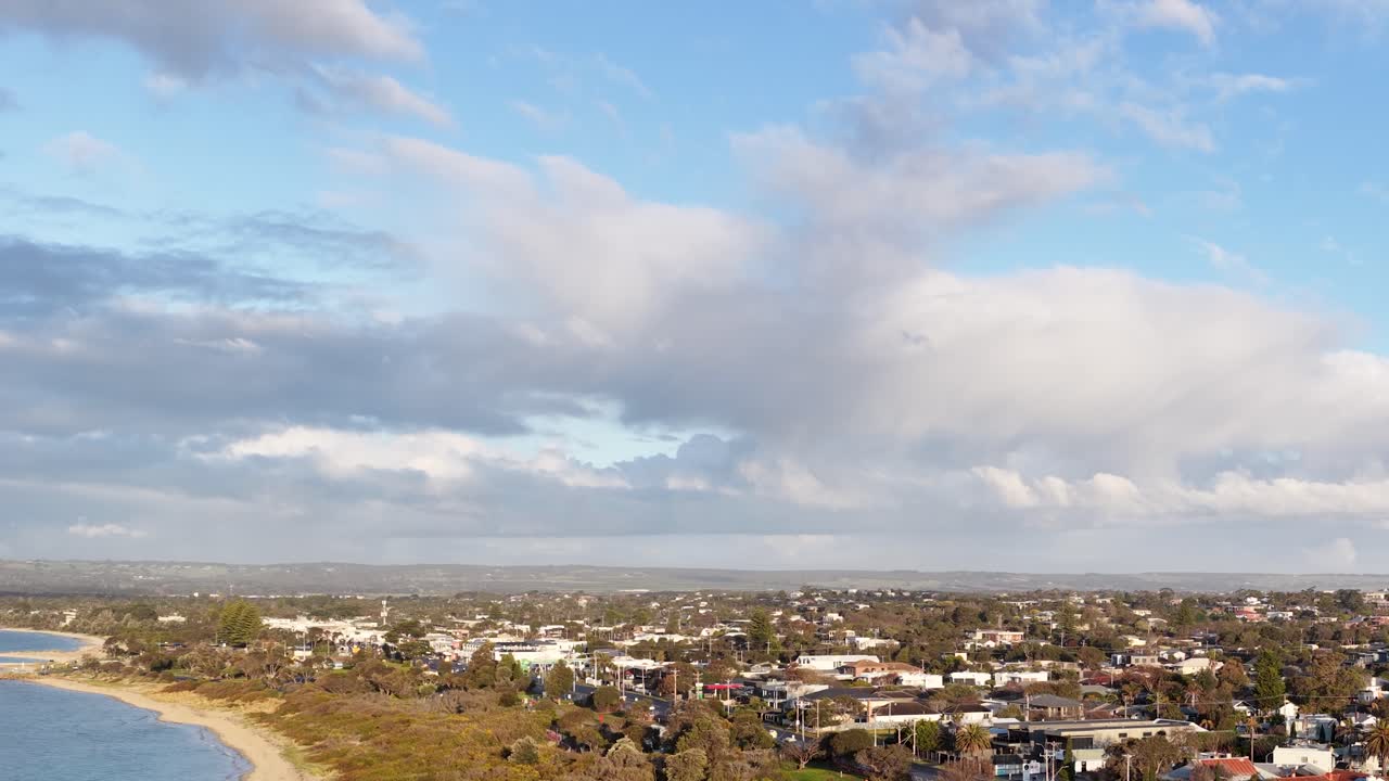 Drone pans above Rye coastline, revealing shoreline, residential area, calm bay, and dramatic sky