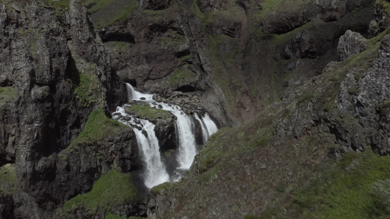 Aerial flying through amazing rugged Icelandic canyon with waterfall