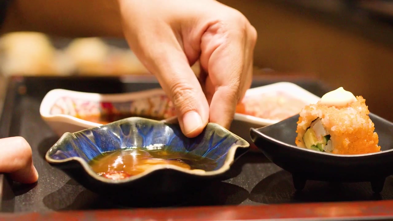 Primo piano di mani che dispongono involtini maki e ciotole di salsa di soia su un vassoio a Bangkok