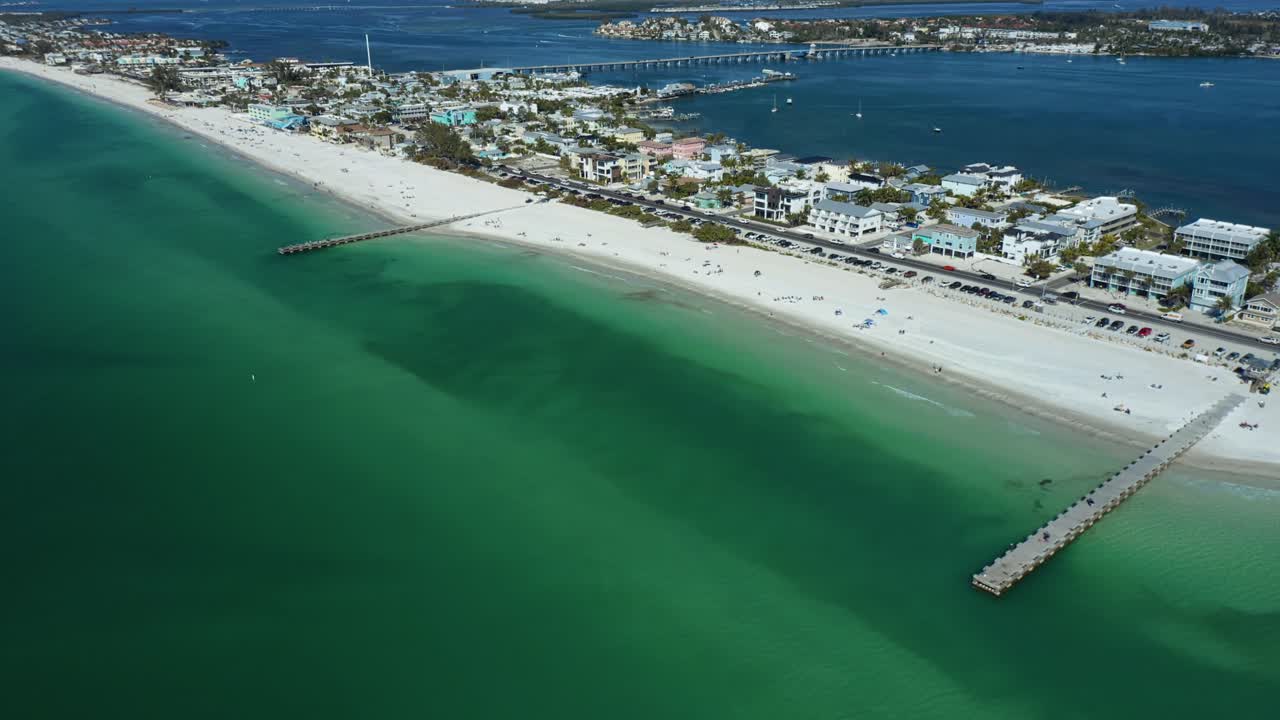 I pontili si estendono nelle limpide acque turchesi di Bradenton Beach, con spiagge di sabbia bianca e case costiere visibili. Ideale per promozioni di viaggio e presentazioni immobiliari.