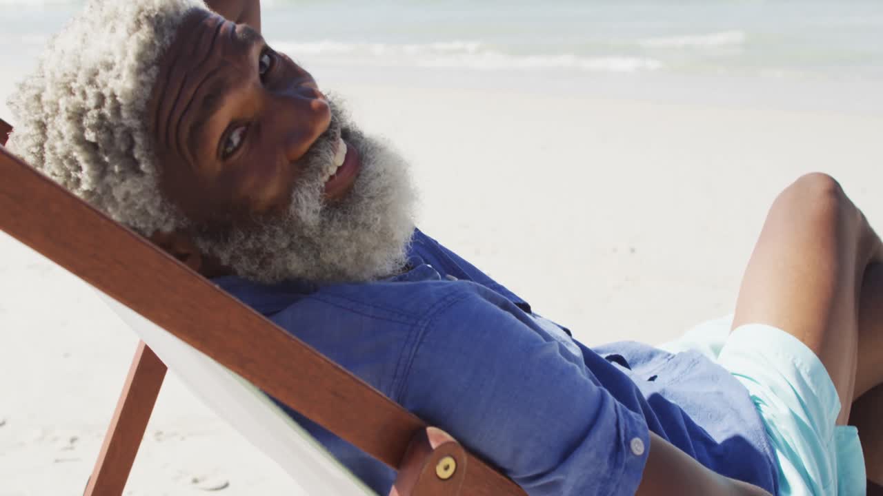 retrato de un anciano afroamericano sonriendo y acostado en una cama de sol en una playa soleada