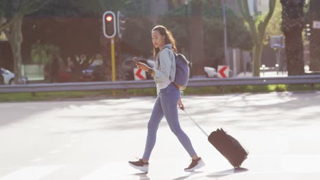 asian woman walking using smartphone and dragging suitcase