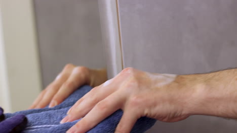 primer plano de una mano masculina caucásica buscando una toalla frente al espejo del baño mientras otra mano la agarra del otro lado