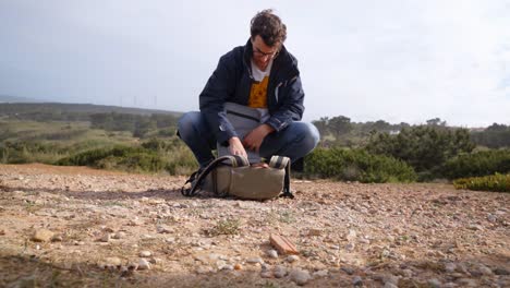 a young man pulling out drone from backpack at a scenic location in portugal