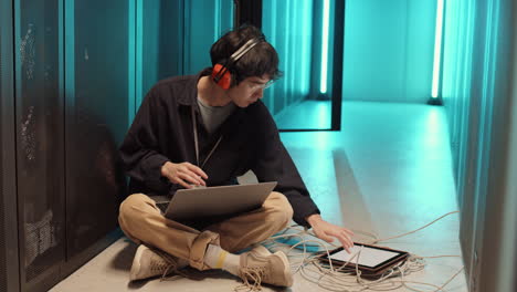 asian it specialist coding on laptop in server room