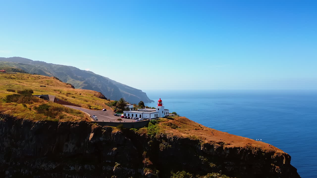 Flying up to a stunning white lighthouse at the dangerous rock. Spectacular view of the Madeira Island coast from top perspective.