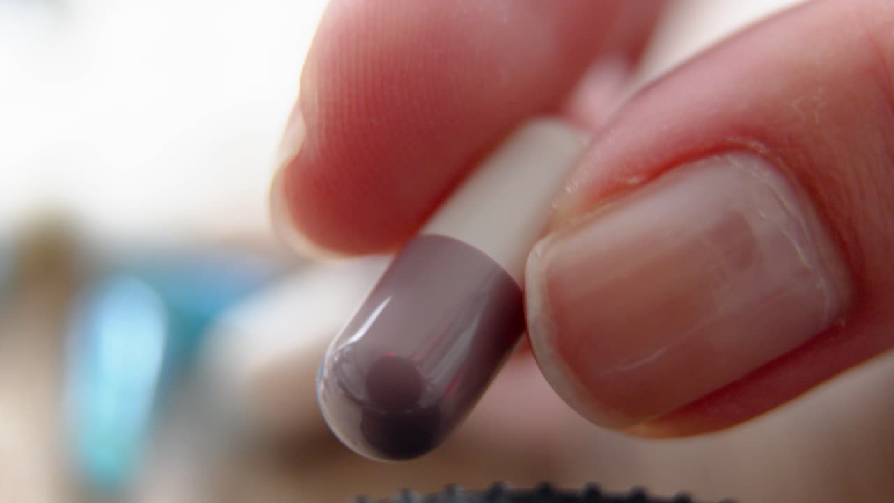 hand gently holds a single capsule pill in natural light closeup