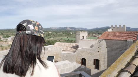 woman looking at phone on castle terrace in valderrobres, spain on a sunny day