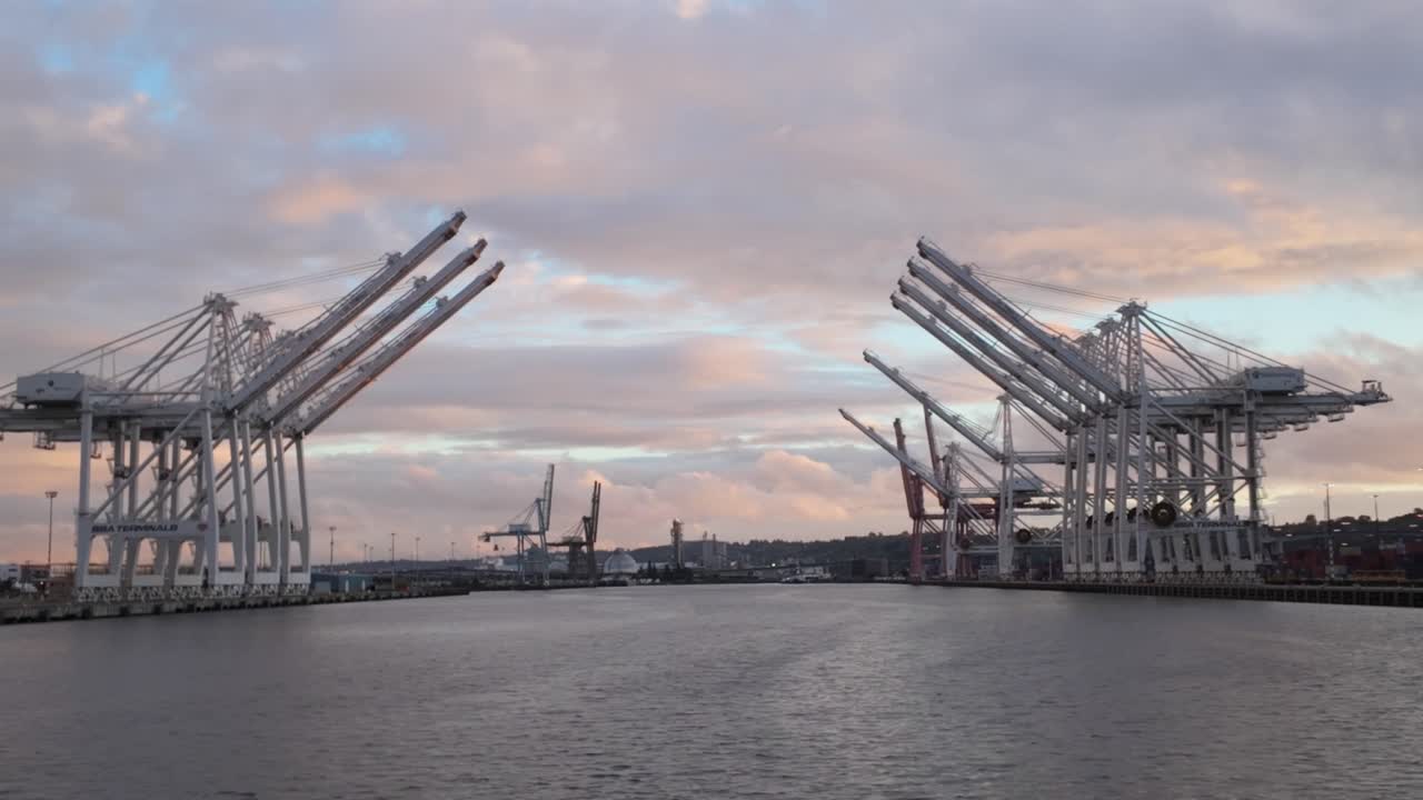 Gimbal wide panning shot of industrial cranes as seen from a moving boat on Elliott Bay during sunset at the Port of Seattle, Washington. 4K at 30 FPS