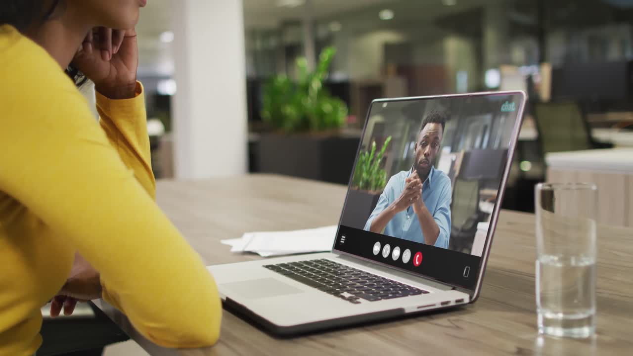 mujer biracial usando computadora portátil para videollamada, con un colega de negocios en la pantalla