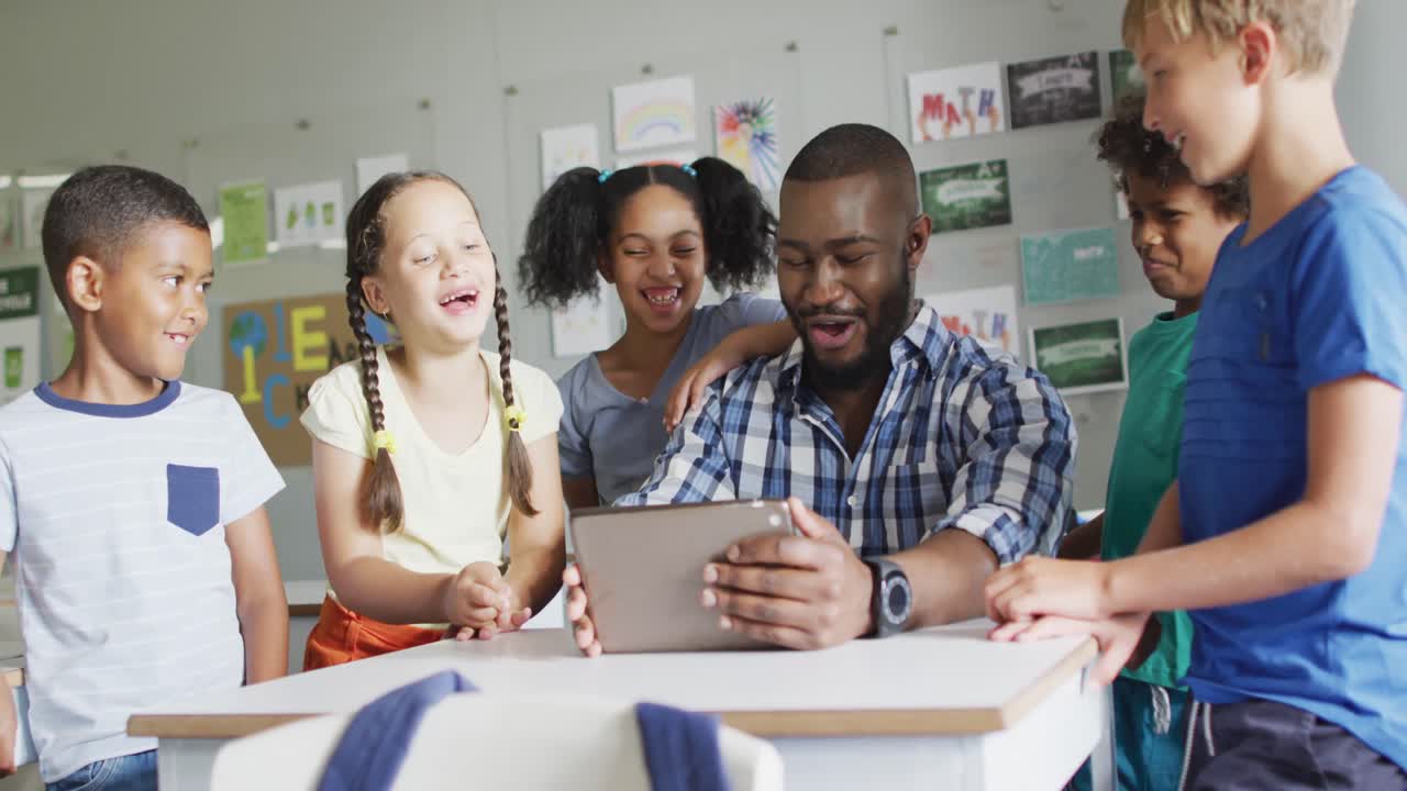 Video of happy african american male teacher and class of diverse pupils working on tablet