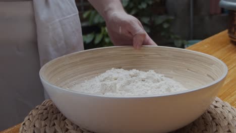 chef pours down water on the pizza dough in a deep plate