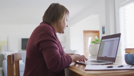 mujer mayor afroamericana sentada en la mesa de comedor usando una computadora portátil