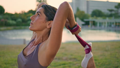 yoga woman stretching leg using elastic band sunset park closeup. lady pilates