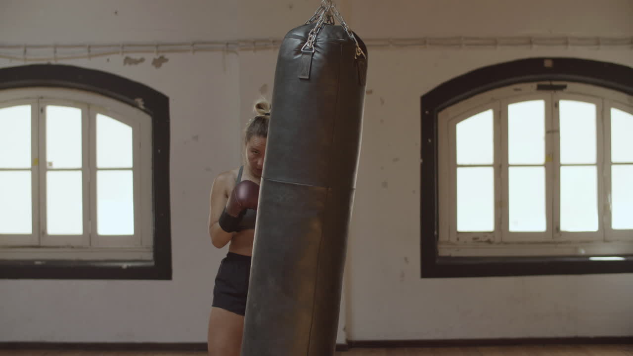 Statische Aufnahme einer fokussierten Boxerin, die im Fitnessstudio auf einen Sandsack schlägt