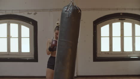 static shot of focused female boxer hitting punching bag in gym