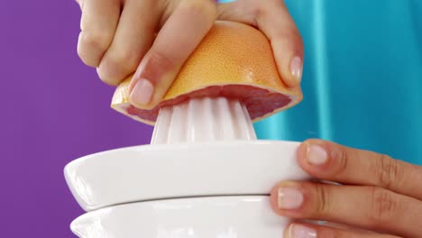 woman preparing blood orange juice from juicer against violet background