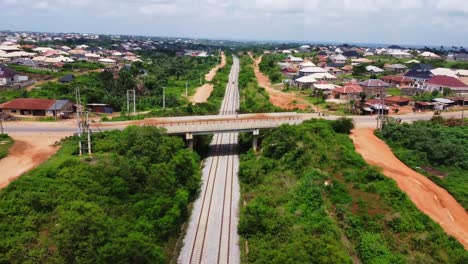 jib down of a long railroad running through a small town in rural nigeria. traffic drives over the bridge crossing the track