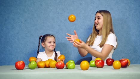 woman and little girl playing with fresh fruits at home. mother and daughter juggle with orange tangerines. organic fruits on the table.