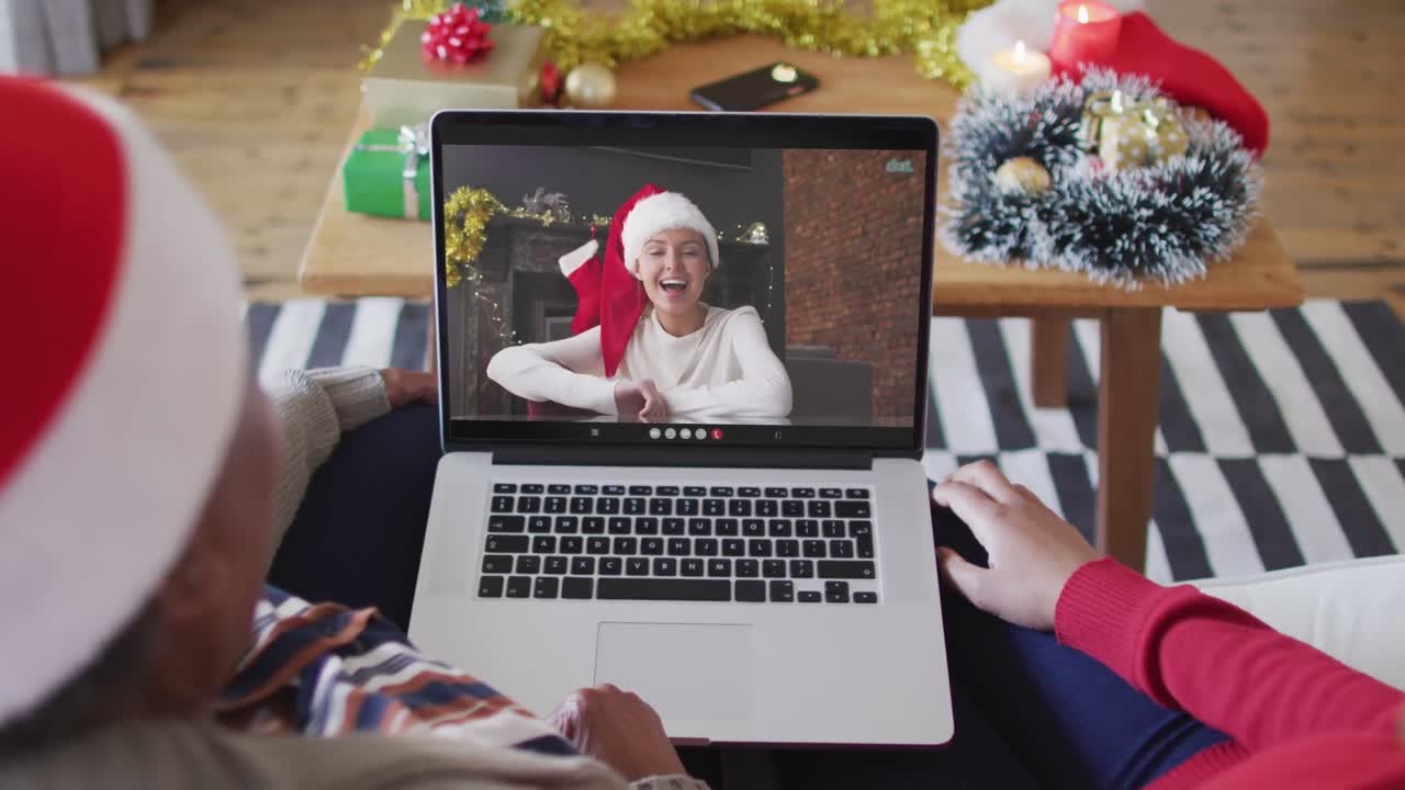 madre y hija afroamericanas usando una computadora portátil para una videollamada de navidad con una mujer en la pantalla