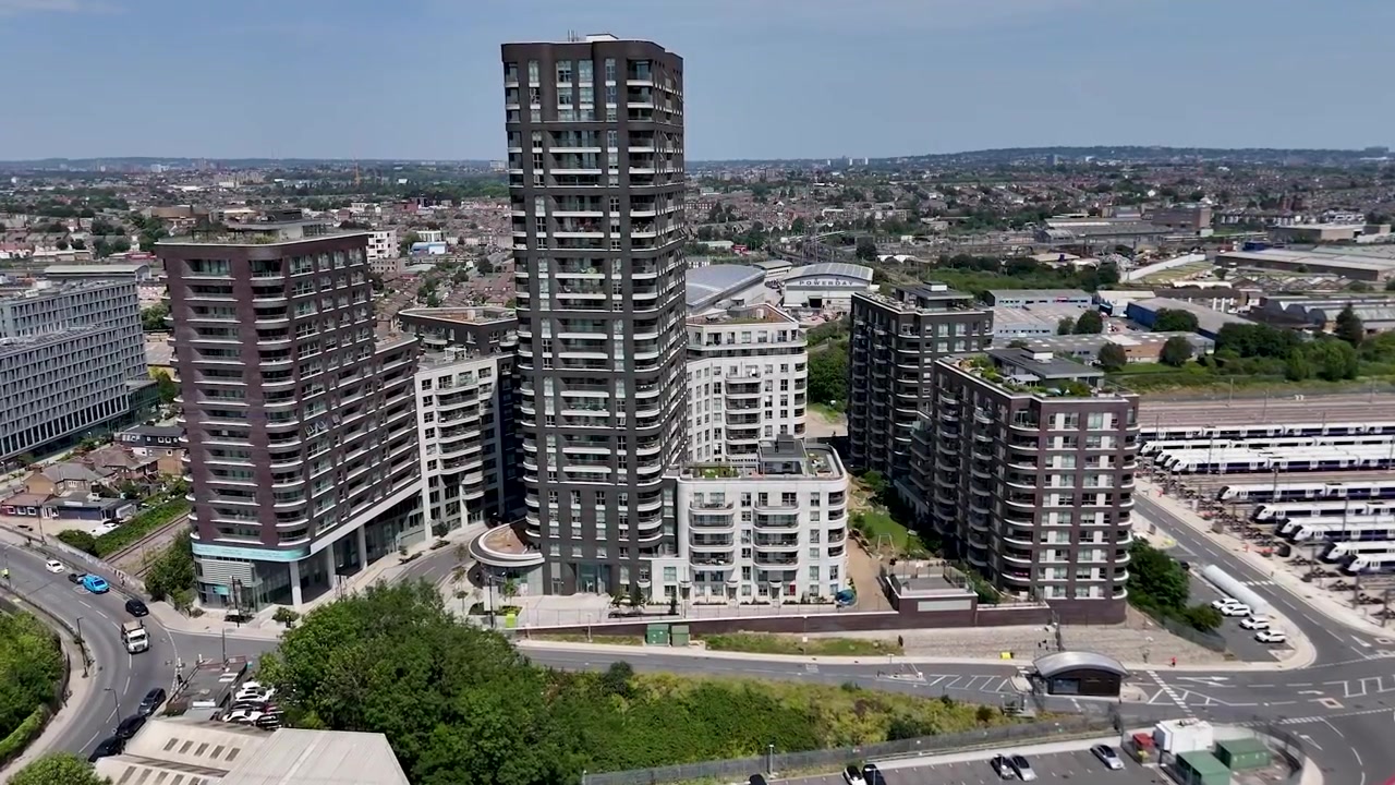 Vista aerea di un nuovo sviluppo residenziale a ovest di Londra, con condomini in mattoni e vetro attorno a una rotonda, con un parcheggio per pullman e terreni ferroviari sullo sfondo.