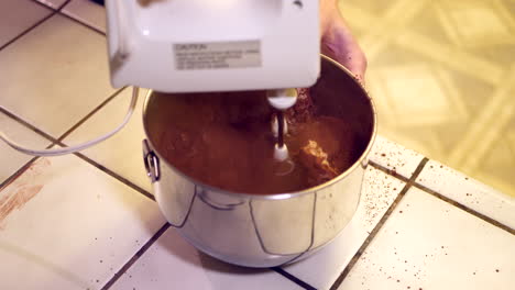 un chef en una cocina usando una batidora eléctrica para hacer masa de pastel de chocolate en un tazón de metal con el polvo haciendo un gran desastre
